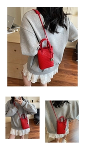 Detail of red woven mini crossbody bag featuring a silver heart charm and slim strap