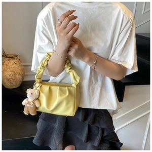 Detail of yellow pleated handbag with soft PU texture and cute plush bear accessory charm