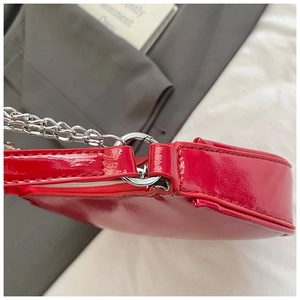 Detail of red patent leather shoulder bag featuring silver chain strap and neat stitching