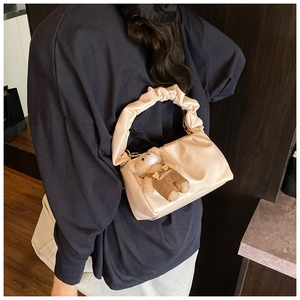 Detail of a beige ruched shoulder bag with a cute plush bear pendant accessory