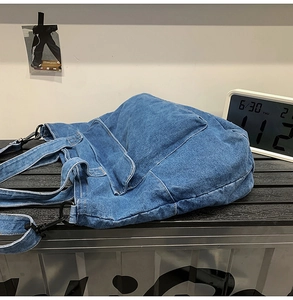 Close-up of blue denim tote bag with functional front flap pocket and black metal buckle
