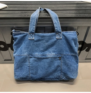 Detailed view of dark blue denim tote bag with stitched pocket and metal zipper closure