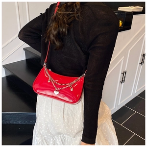 Detail of red patent leather shoulder bag with silver chains and heart charm