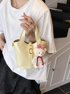 Elegant beige glossy bucket bag with a plush bear charm and metallic buckle accent
