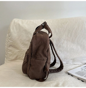 Side view of dark brown canvas backpack with side pocket on a white fabric sofa