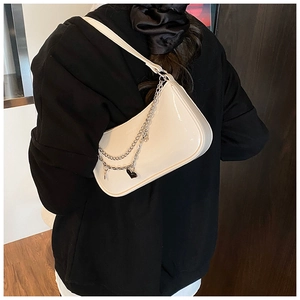 Detail view of glossy white patent leather shoulder bag with silver heart chain pendant