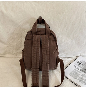 Detailed back view of a brown canvas backpack with wide straps and top handle for women