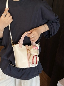 Chic cream and pink bucket bag with gold buckle and plush bear pendant on model