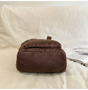 Detailed view of the dark brown canvas backpack with a side zipper and textured fabric
