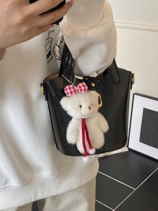 Chic black glossy bucket bag with golden hardware and white plush bear charm accessory