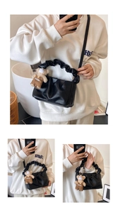 Detail of black pleated cloud bag with stylish bear pendant and long shoulder strap