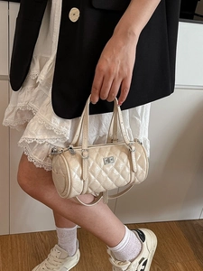 Sac Boston matelassé en similicuir crème avec fermoir argenté porté par un mannequin