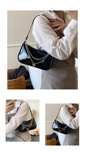 Detail of black patent leather underarm bag with silver heart charms and chain