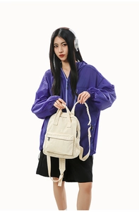 Detail view of cream canvas backpack featuring top handles and front pocket for commute
