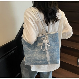 Dettaglio della borsa tote in denim blu con catene argentate e ciondolo a fiocco decorativo