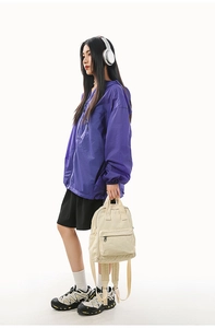 Outdoor street style with a compact cream canvas backpack and purple hooded jacket