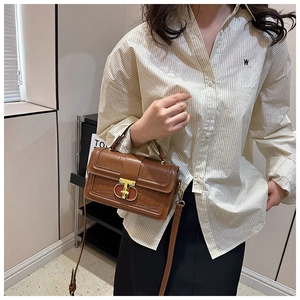 Detail of caramel brown croc-effect handbag with vintage metal buckle on striped shirt