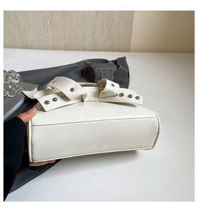 Détail du sac blanc à clous avec rabat à nœud créatif et cuir PU lisse et brillant