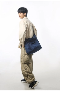 Detail view of a large denim tote bag with front flap pocket and adjustable strap on a model