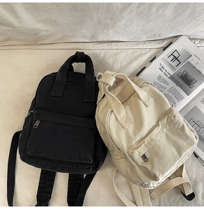 Overhead view of black and beige canvas mini backpacks on white fabric background