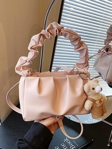 Pink pleated cloud handbag with ruffle handle and cute teddy bear charm on black desk