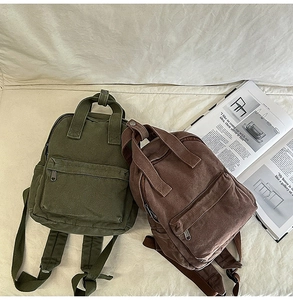 Detail view of olive green and brown canvas backpacks on a beige background
