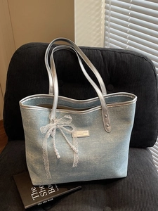 Borsa tote in denim azzurro con manici argento e fiocco di perle su sedia nera