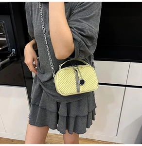 Détail d'un sac bandoulière jaune tressé avec chaîne argentée et pompon sur un mannequin