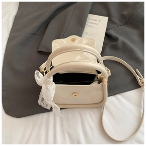 Detail of a cream fashion handbag with a decorative white lace bow and gold magnetic buckle