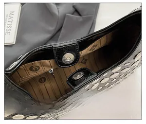 Detailansicht der Magnetschnalle und Silbernieten auf schwarzer Ledertasche mit Logo-Futter