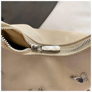 Détail d'un sac en cuir crème avec fermeture éclair argentée et ornement papillon en métal