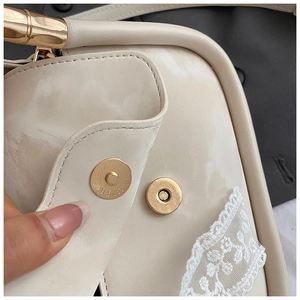 Macro shot of cream handbag featuring white lace trim and gold bamboo-style handle detail