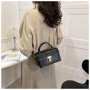 Detail of black crocodile texture handbag with gold metal clasp on female model