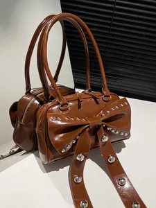 Sac à main en cuir verni marron avec grand nœud et rivets sur socle blanc pur