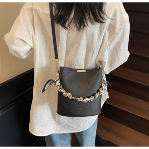 Detail of black leather bucket bag with polka dot scarf wrapped chain handle and gold bar