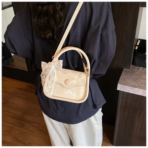 Close-up of cream square bag featuring white lace bow detail and slim shoulder strap