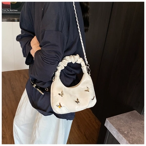 Sac à main blanc plissé avec papillons métalliques présenté dans un décor d'intérieur