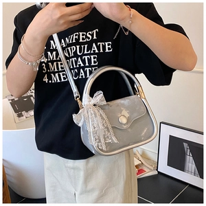 Detail of silver metallic handbag with lace bow ornament and curved handle shown on model