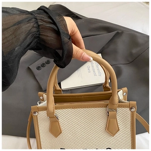 Dettaglio borsa tote in paglia intrecciata con manici in pelle marrone e tessuto