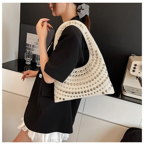 Schicke cremeweiße Nieten-Schultertasche mit silbernen Bolzen an einem Model in einem Raum