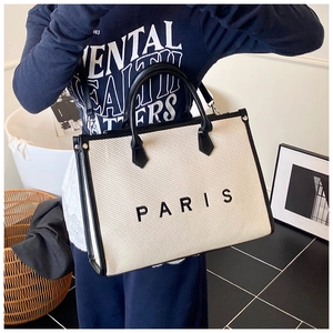 Detailed close-up of large canvas tote bag with black leather trim and Paris text print