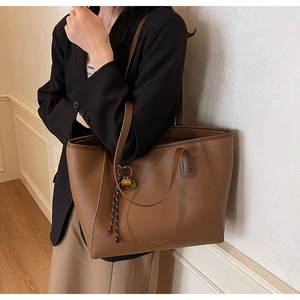 Detail of a brown lychee pattern leather tote bag with woven knot and metal pendant decor