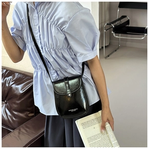 Detail of a black glossy crossbody bag with white fashion text on the buckle closure