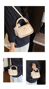 Detail of a beige saddle bag with lace bow charm and adjustable shoulder strap
