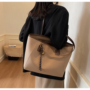 Close-up of beige lychee leather tote bag with contrast brown handles and woven charm