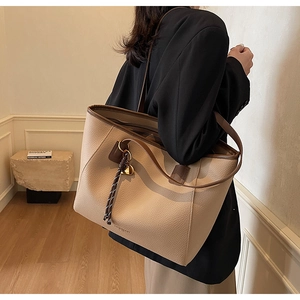 Detail of beige litchi grain tote bag featuring dark brown straps and woven pendant