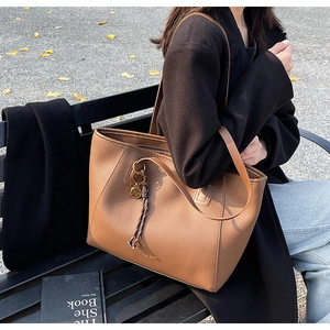 Detailed view of brown lychee grain leather tote bag with metal charm in outdoor setting