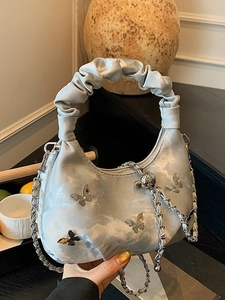 Sac plissé bleu avec papillons métalliques et anse froncée, présenté à la main