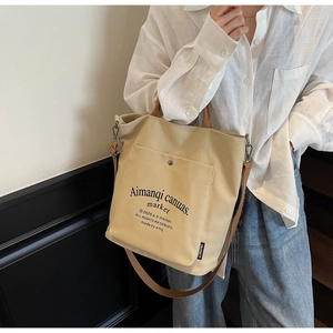 Detail of beige canvas tote bag showing front pocket with button and brown strap