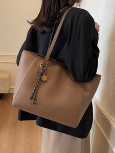 Brown large leather tote bag with shoulder strap and woven pendant in minimalist room